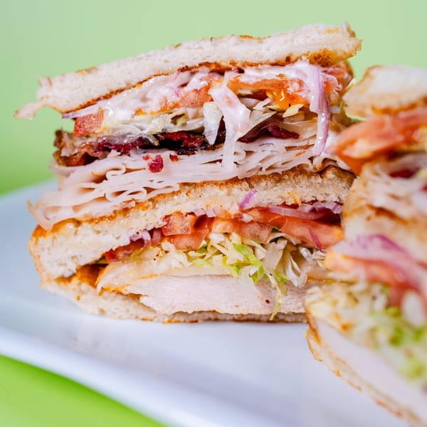A large, layered sandwich with turkey, bacon, lettuce, tomato, and sauce on toasted bread.