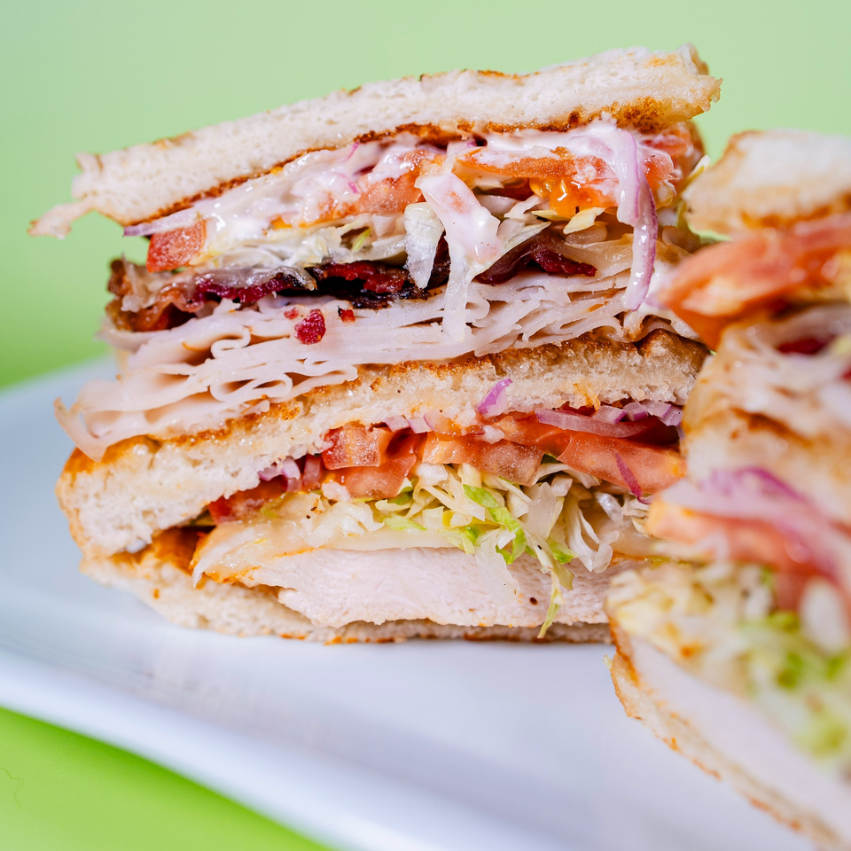 A large, layered sandwich with turkey, bacon, lettuce, tomato, and sauce on toasted bread.