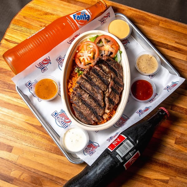 Grilled steak and rice bowl with tomatoes, sauces, Fanta, and Coca-Cola on a tray.