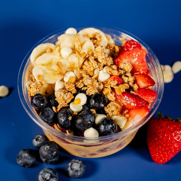 A vibrant acai bowl from Clutch City Kitchen, topped with bananas, blueberries, strawberries, and granola.