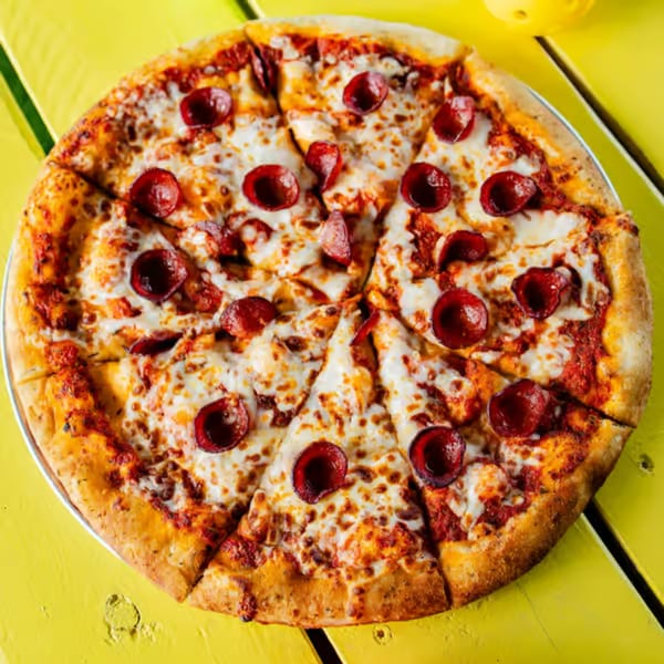 Clutch City Kitchen's pepperoni pizza, sliced and ready to eat, on a bright yellow table.