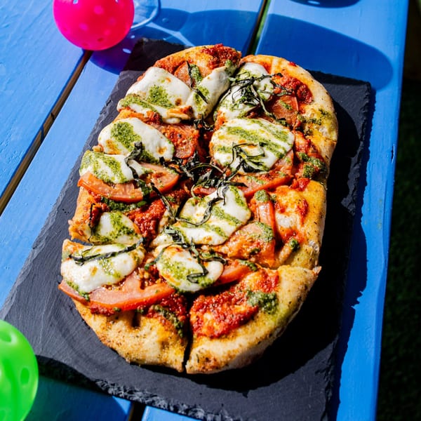 Clutch City Kitchen's rectangular pizza with pesto, mozzarella, and tomatoes on a blue table.