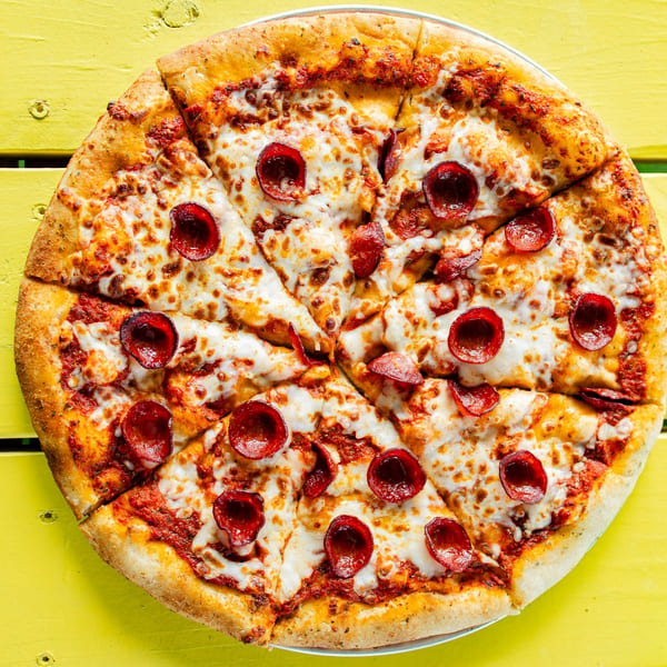 A whole pepperoni pizza, sliced into eight pieces, on a bright yellow wooden table.