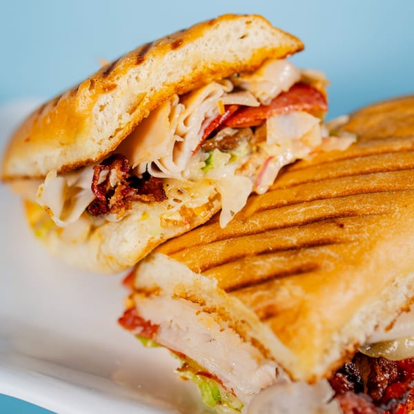 Close-up of a grilled panini sandwich, cut in half, revealing turkey, pepperoni, bacon, and cheese.