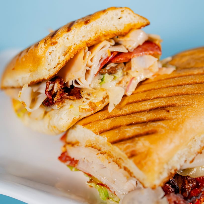 Close-up of a grilled panini sandwich, cut in half, revealing turkey, pepperoni, bacon, and cheese.