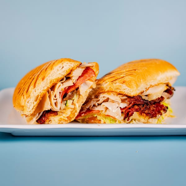 A sliced panini sandwich with meat, cheese, and lettuce on a white plate against a blue background.