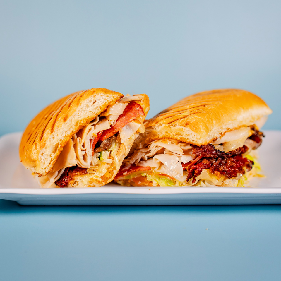 A sliced panini sandwich with meat, cheese, and lettuce on a white plate against a blue background.