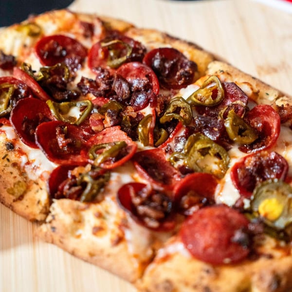 Clutch City Kitchen's pepperoni, jalapeño, and bacon pizza on a wooden board.