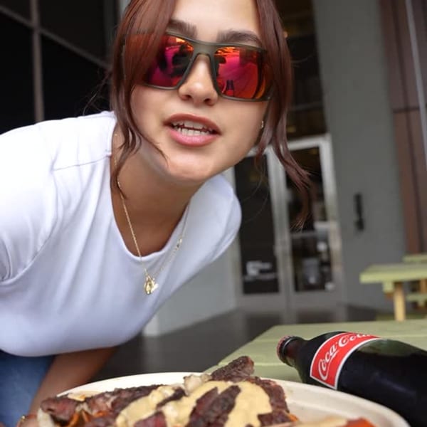 A woman in sunglasses leans over a plate of food and a Coca-Cola bottle.