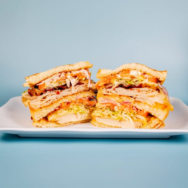 Two halves of a large, layered sandwich with turkey, bacon, lettuce, tomato, and sauce.