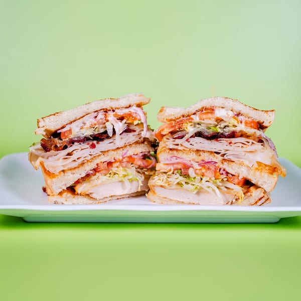 Two halves of a large, layered club sandwich with turkey, bacon, lettuce, tomato, and onion.