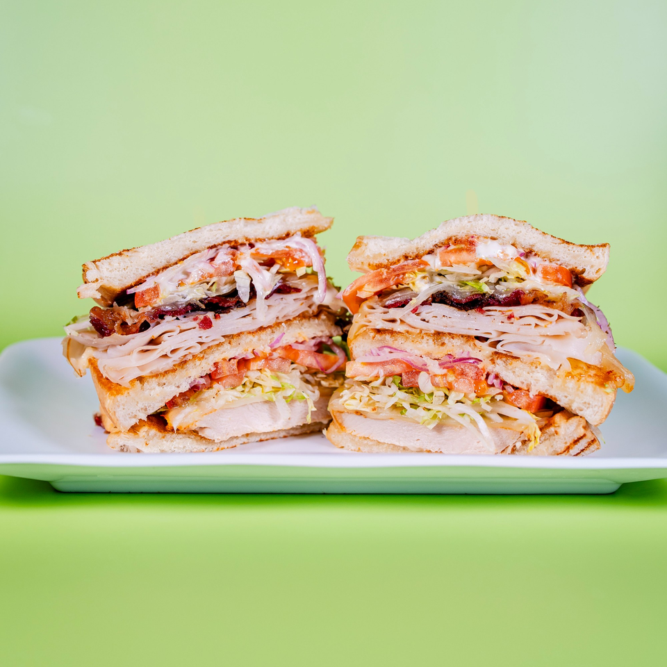 Two halves of a large, layered club sandwich with turkey, bacon, lettuce, tomato, and onion.