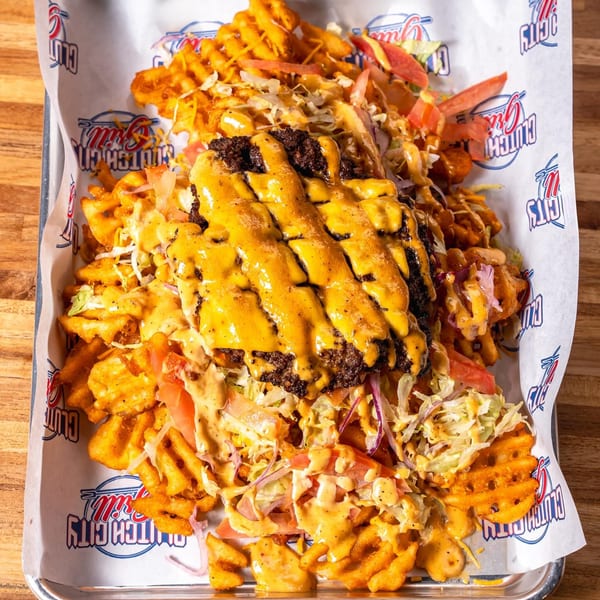 A large serving of waffle fries topped with a burger patty, melted cheese, and fresh vegetables.