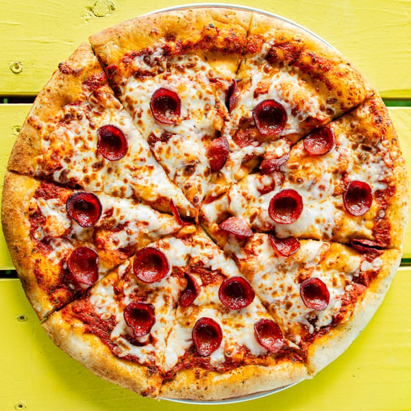 A whole pepperoni pizza from Clutch City Kitchen, sliced and ready to eat on a bright yellow table.