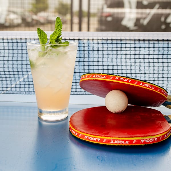 A refreshing drink with mint and ice next to two red ping pong paddles and a ball.