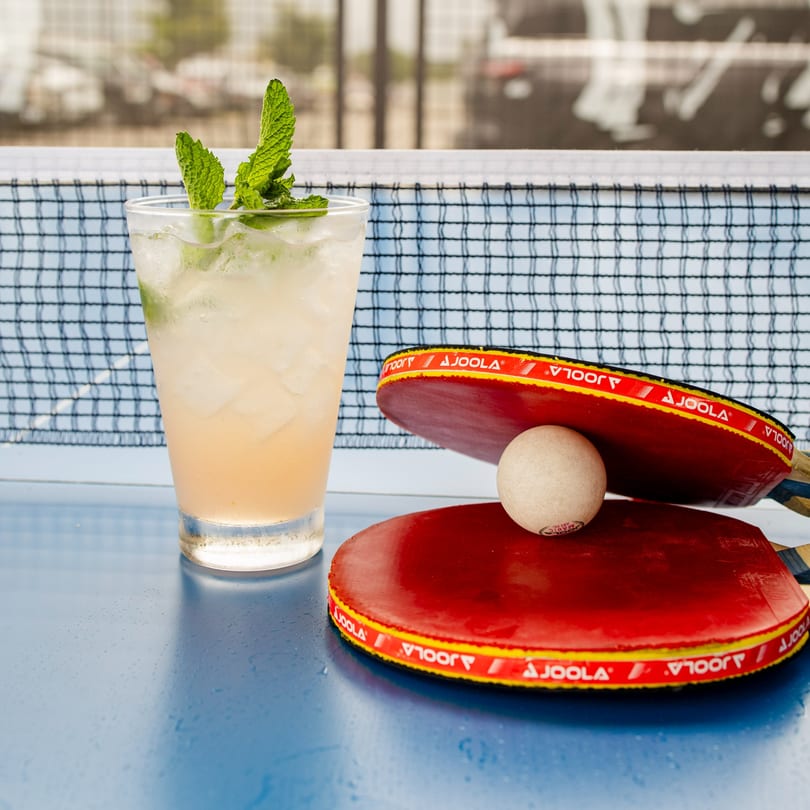 A refreshing drink with mint and ice next to two red ping pong paddles and a ball.