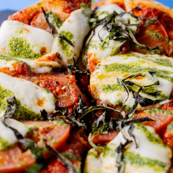 Close-up of a Clutch City Kitchen pizza with fresh mozzarella, pesto, basil, and tomato slices.