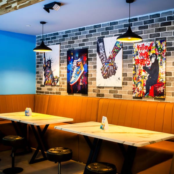 Clutch City Kitchen's dining area with orange booths, marble tables, and pop art on a brick wall.