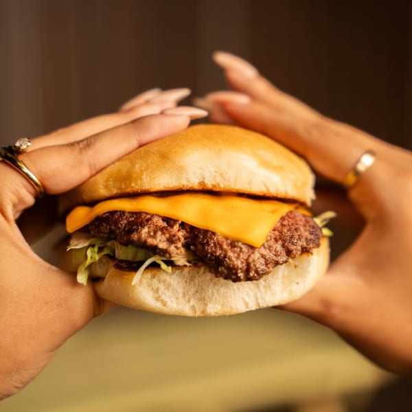 Hands holding a burger with a patty, melted cheese, and lettuce on a bun.