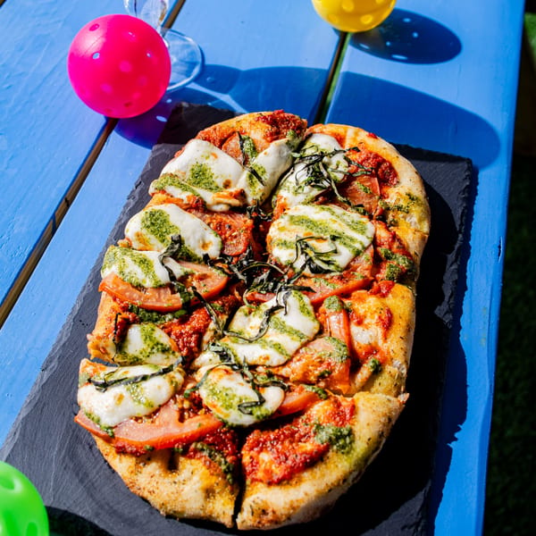 Clutch City Kitchen's flatbread pizza with pesto, mozzarella, tomatoes, and basil on a blue table.