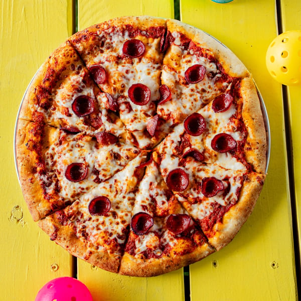 Clutch City Kitchen pepperoni pizza, sliced and ready to eat, on a bright yellow table.