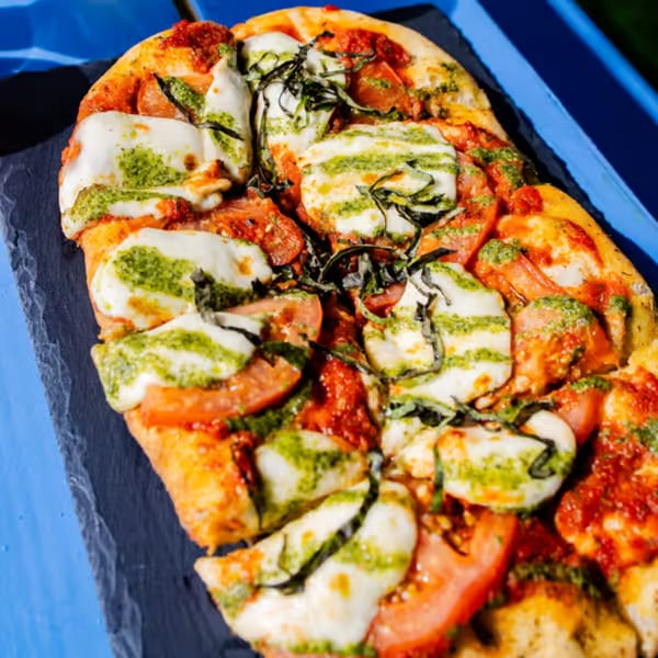 Clutch City Kitchen's flatbread pizza with pesto, mozzarella, tomatoes, and basil on a dark platter.