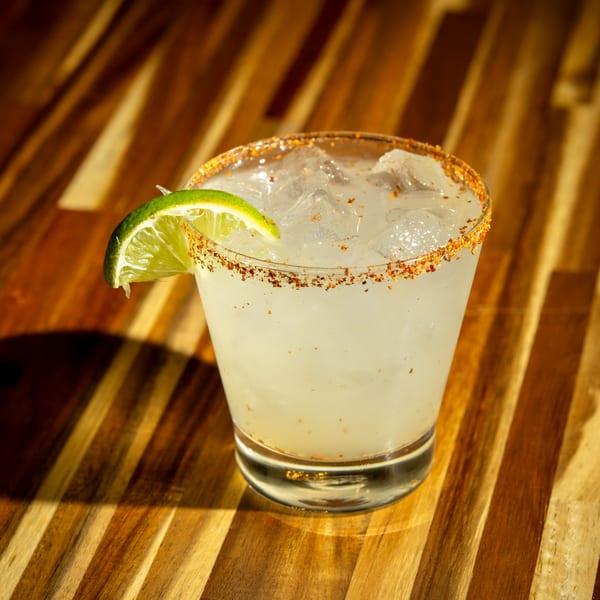 Margarita with a chili-lime rim and a lime wedge, on a wooden table at Clutch City Kitchen.