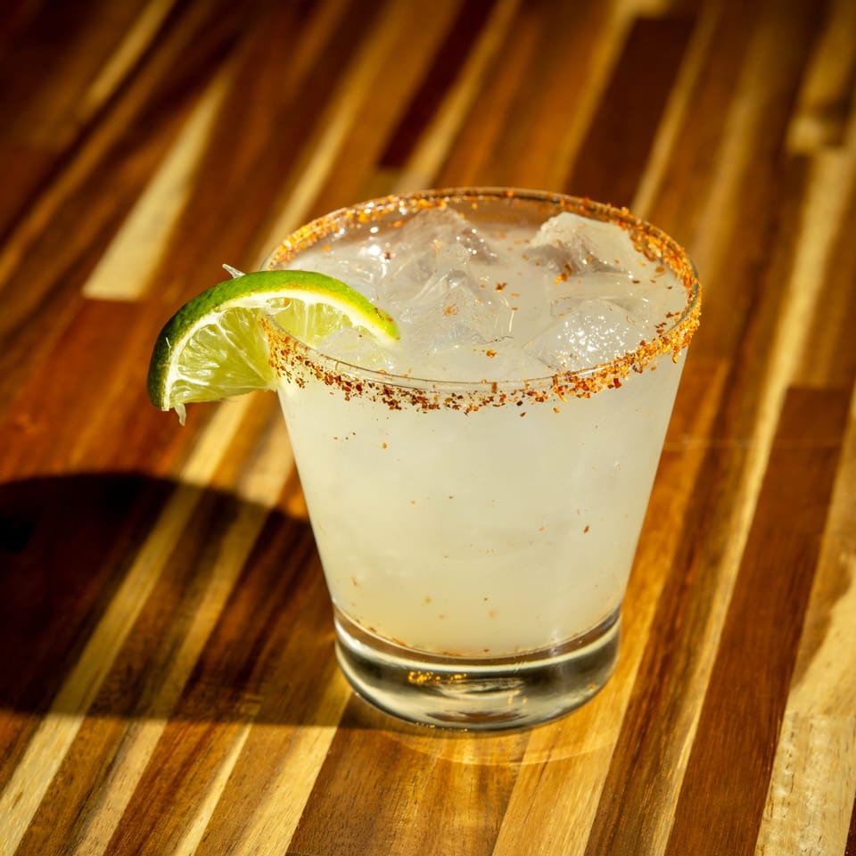 Margarita with a chili-lime rim and a lime wedge, on a wooden table at Clutch City Kitchen.