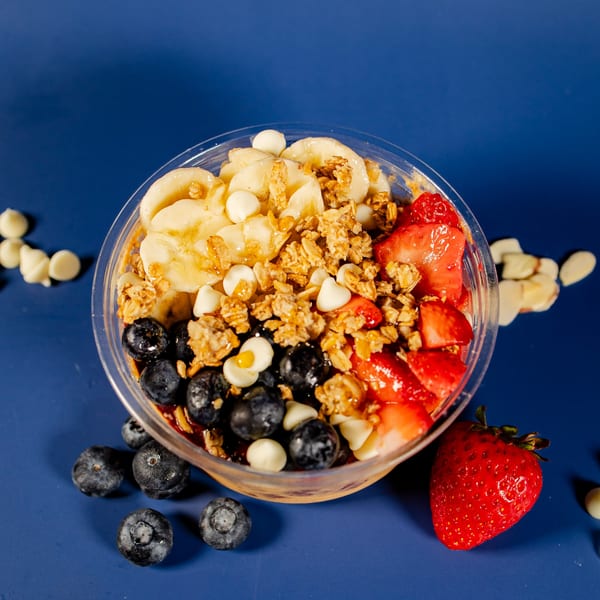 A colorful acai bowl from Clutch City Kitchen, topped with bananas, blueberries, strawberries, granola, and white chocolate chips.
