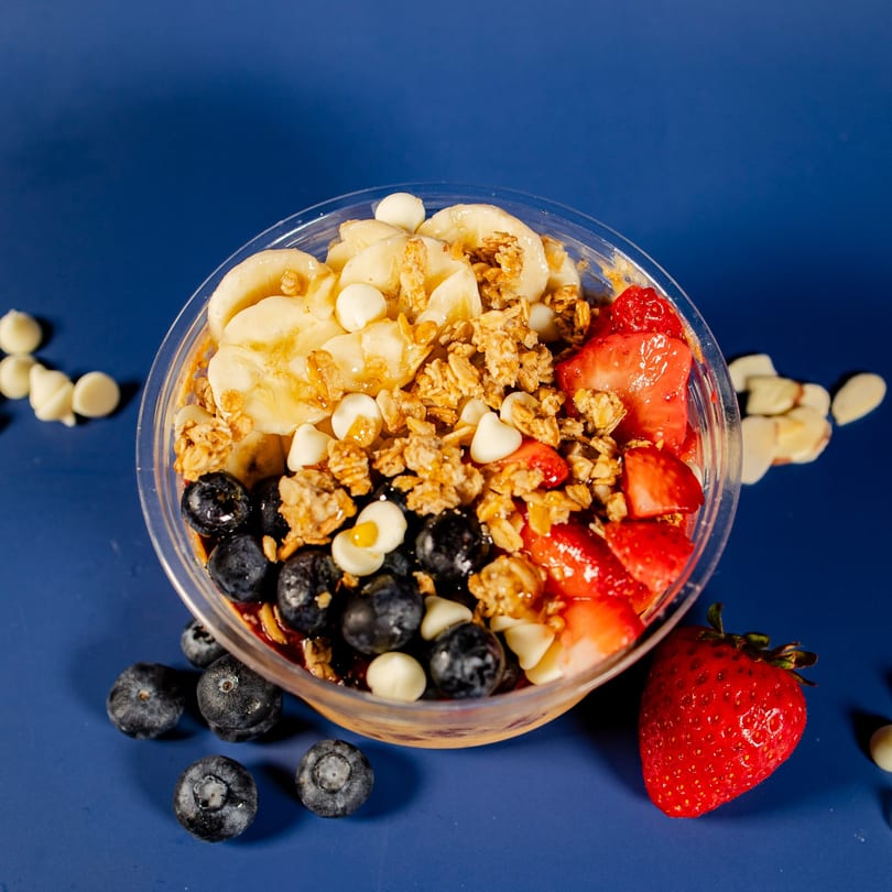 A colorful acai bowl from Clutch City Kitchen, topped with bananas, blueberries, strawberries, granola, and white chocolate chips.